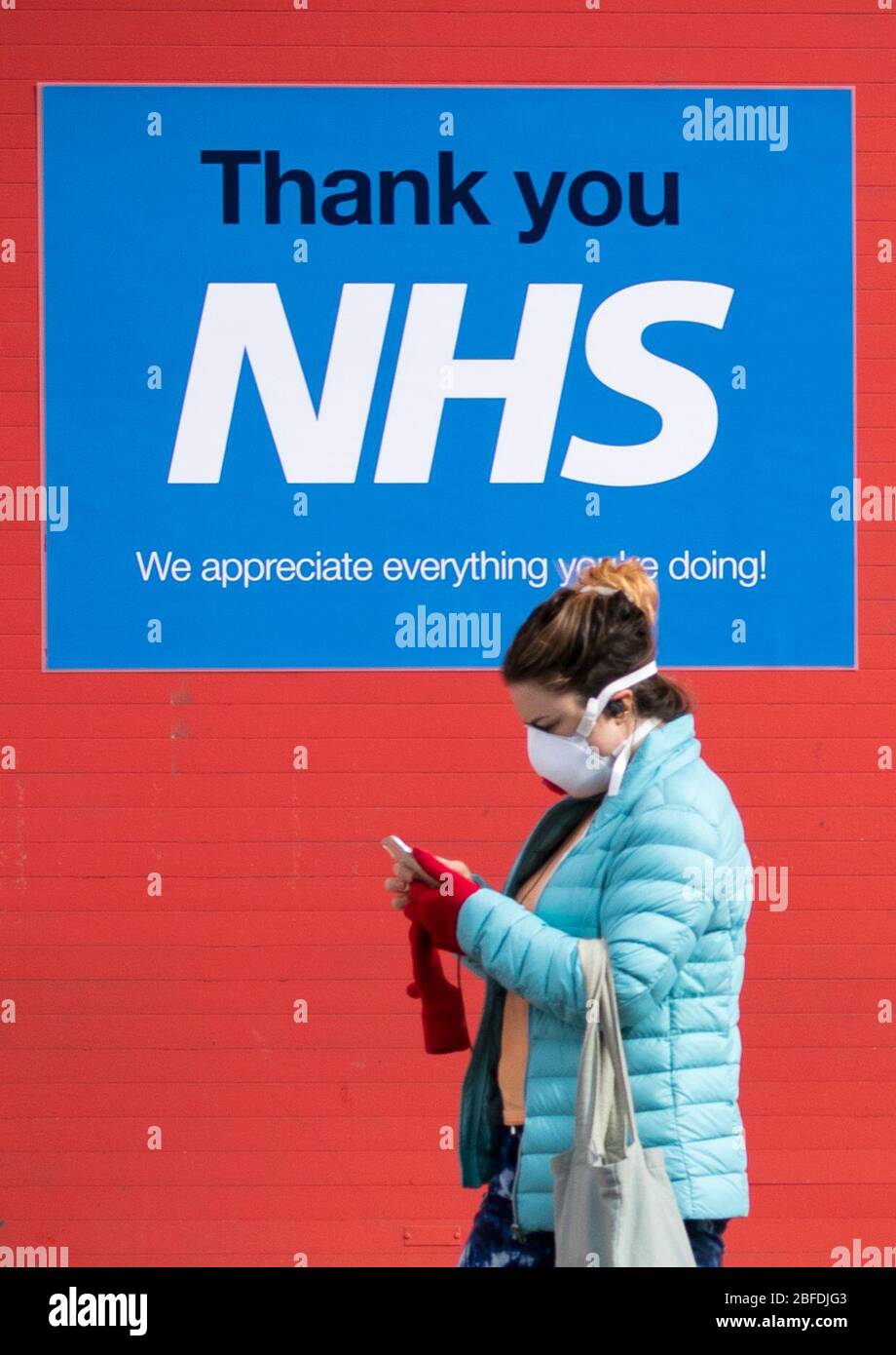 A woman wearing a protective face mask walks past a poster thanking the NHS in Edinburgh as the UK continues in lockdown to help curb the spread of the coronavirus. Stock Photo