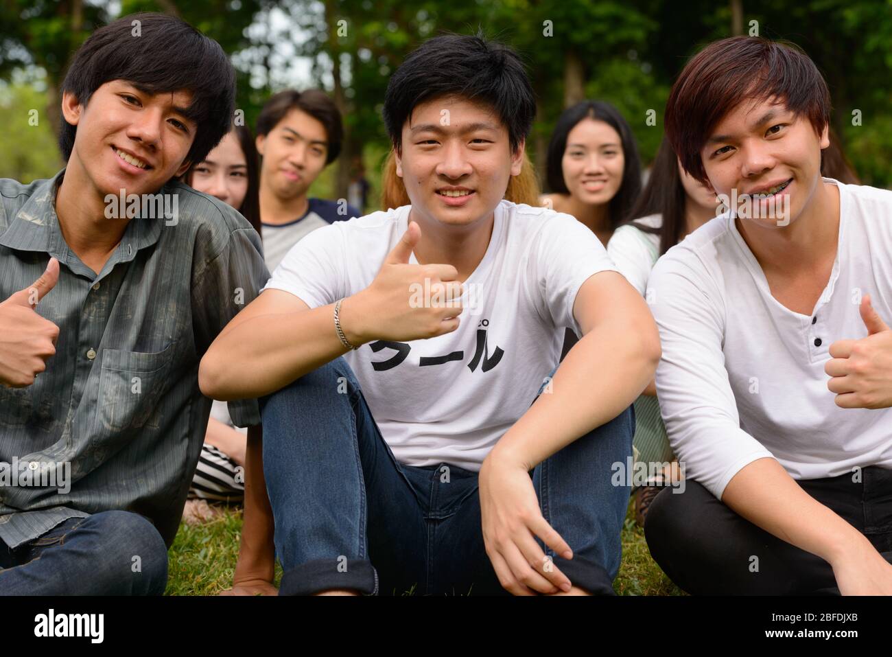 Happy young group of friends giving thumbs up together at the park ...