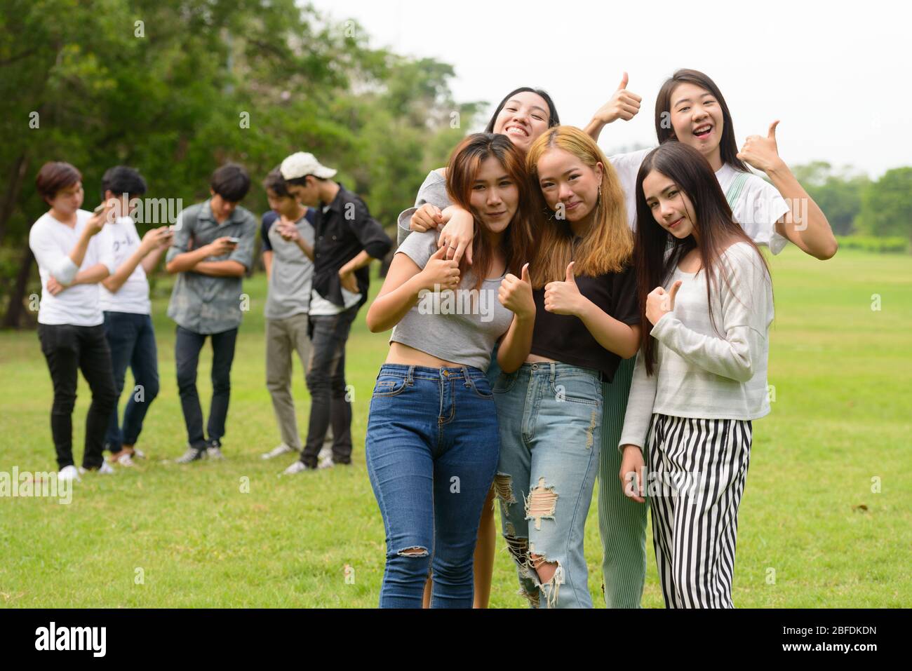 Happy young group of friends giving thumbs up together at the park ...