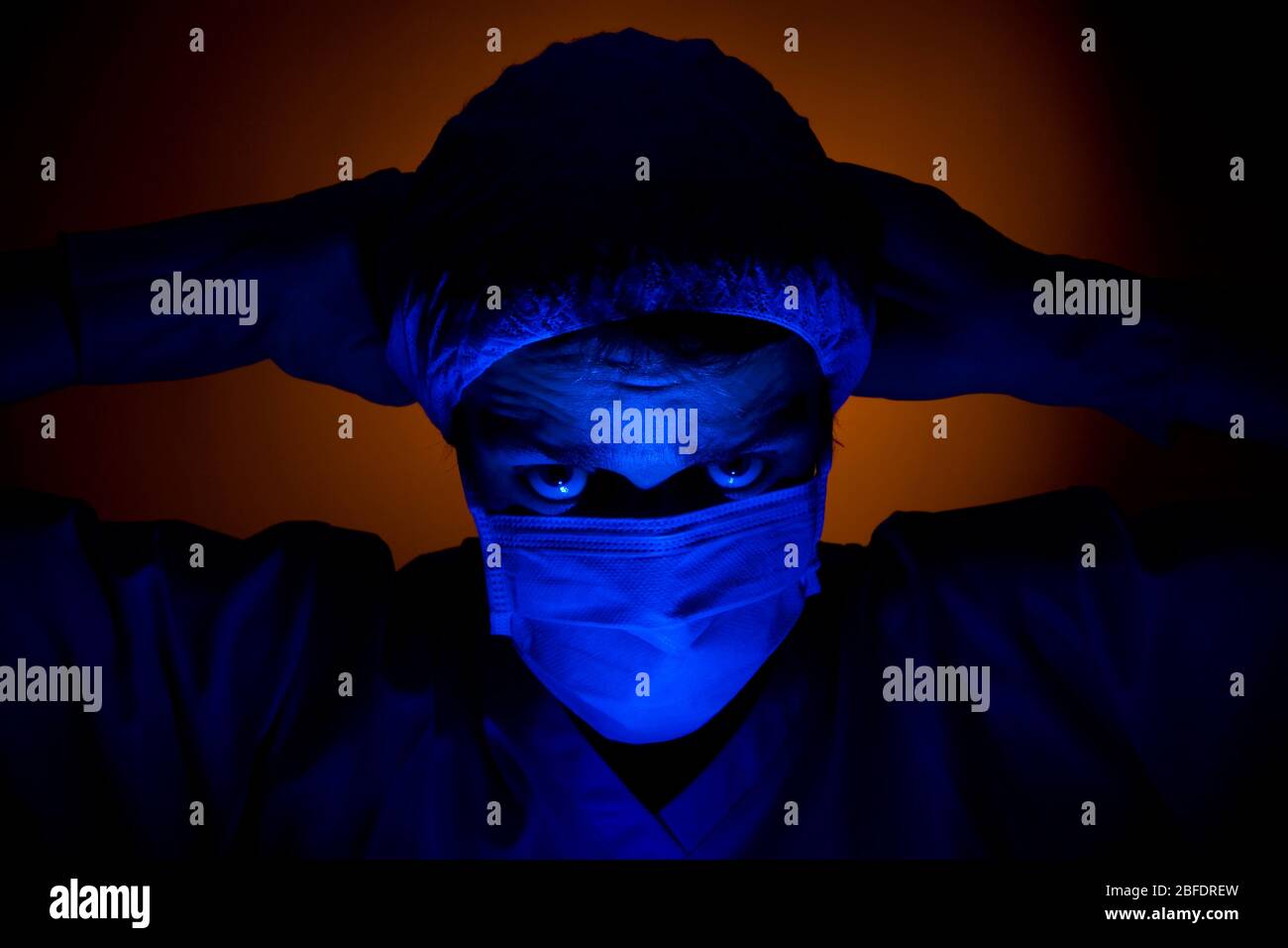 An evil looking masked surgeon, with his hands behind his head. Stock Photo