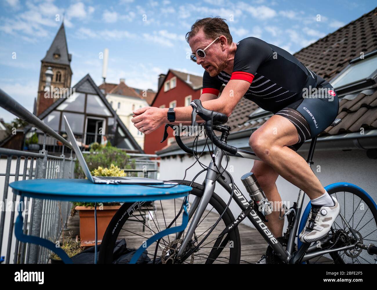Herdecke, Germany. 18th Apr, 2020. Jan Postberg, hobby cyclist, trains with his racing bike on his neighbour's balcony and looks at his laptop, on which he is riding along with several hundred other users on a virtual training track at the same time using the simulation program 'Zwift'. Credit: Bernd Thissen/dpa/Alamy Live News Stock Photo