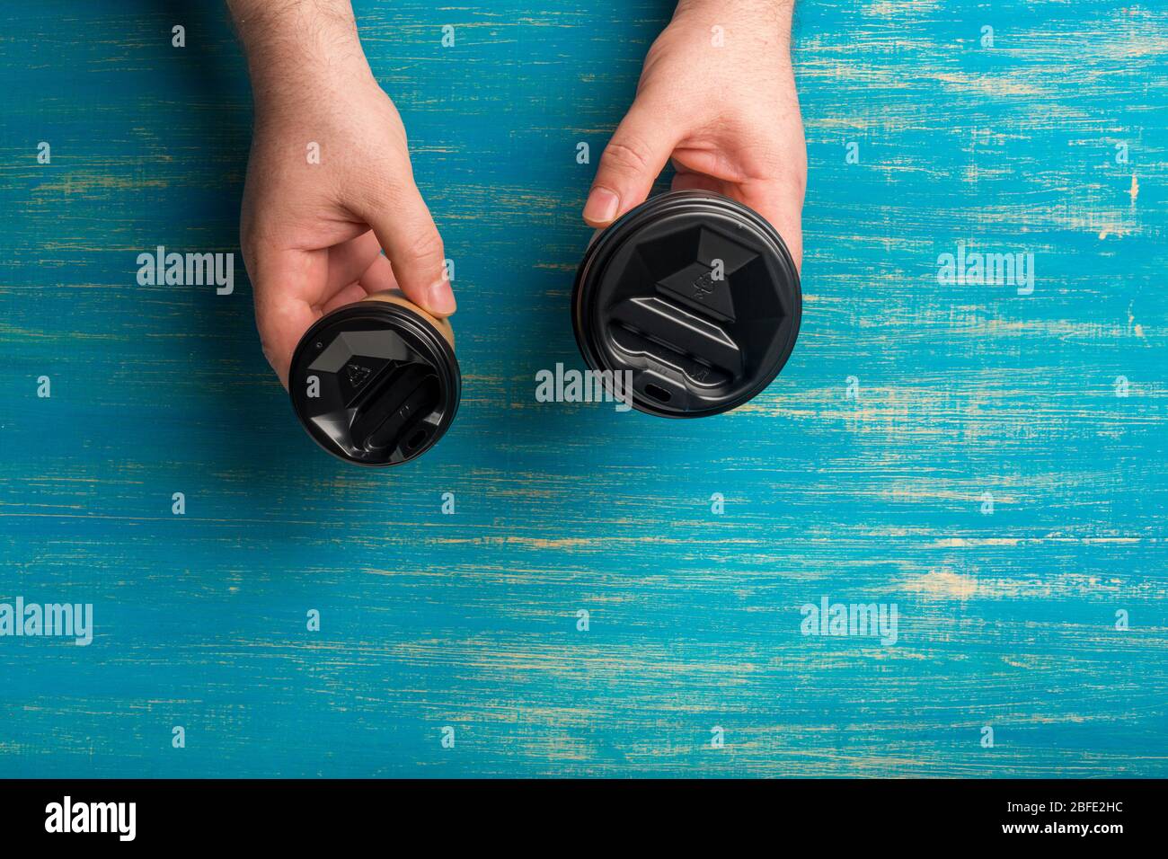 Two disposable paper cups for coffee in a male hand's on a blue wooden background. Stock Photo