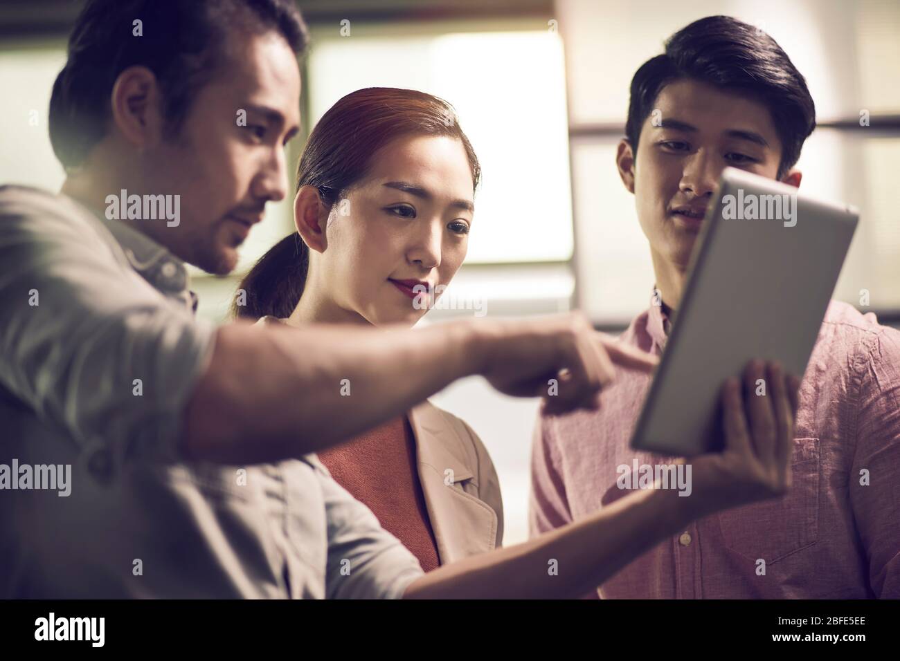 three young asian businessmen entrepreneurs working together in office looking at digital tablet Stock Photo