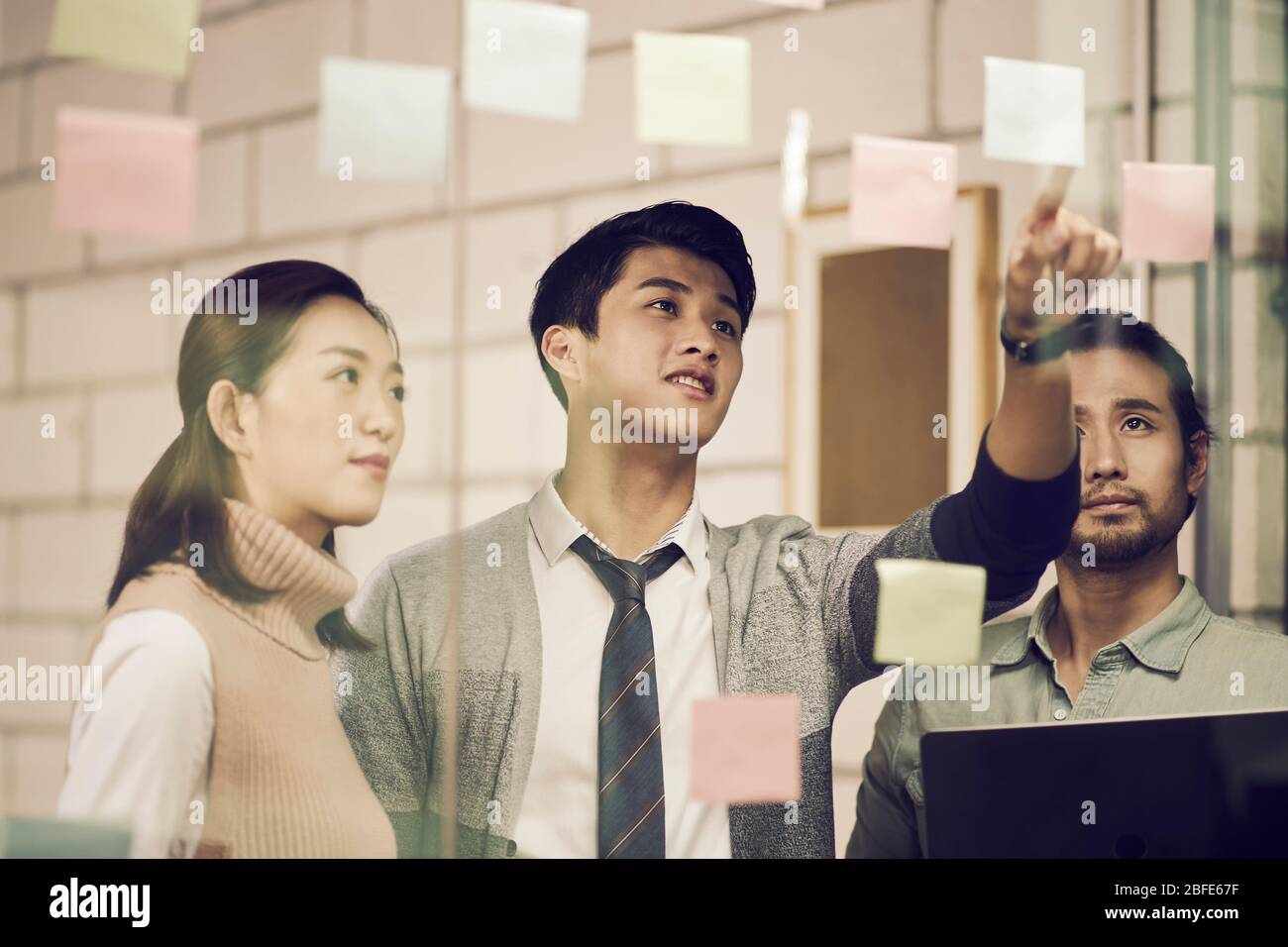 three asian small company businesspeople young entrepreneurs meeing discussing in office using sticky notes Stock Photo
