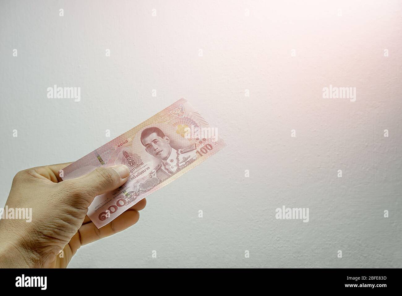 A mans hand is holding one 100 bank notes on a white background. Concept Thai baht currency banknote Stock Photo