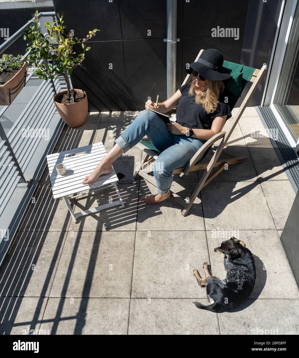 Blonde woman in hat sitting on sunny terrace with dog Stock Photo - Alamy