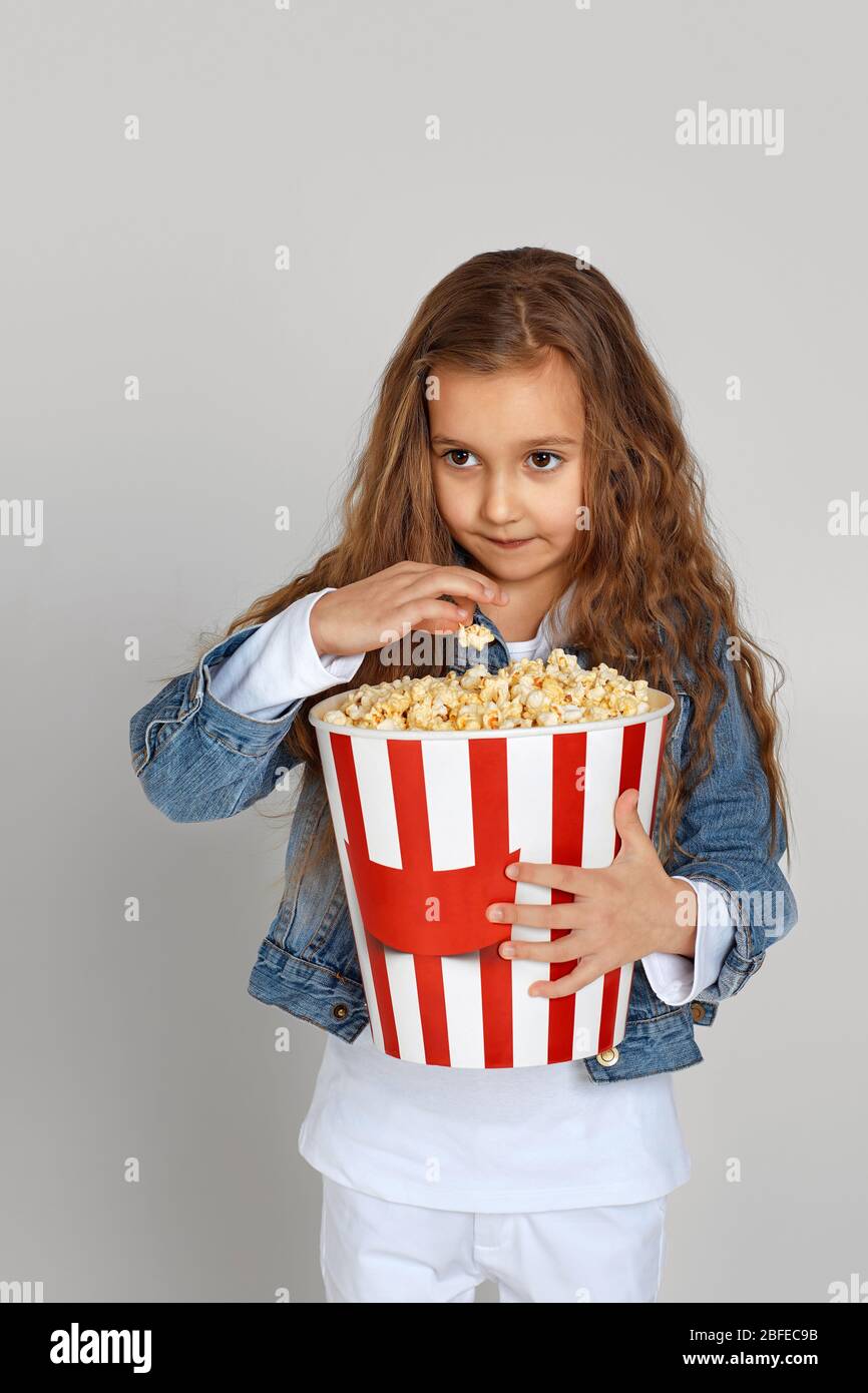 cute child girl having fun and holding popcorn bucket isolated on gray