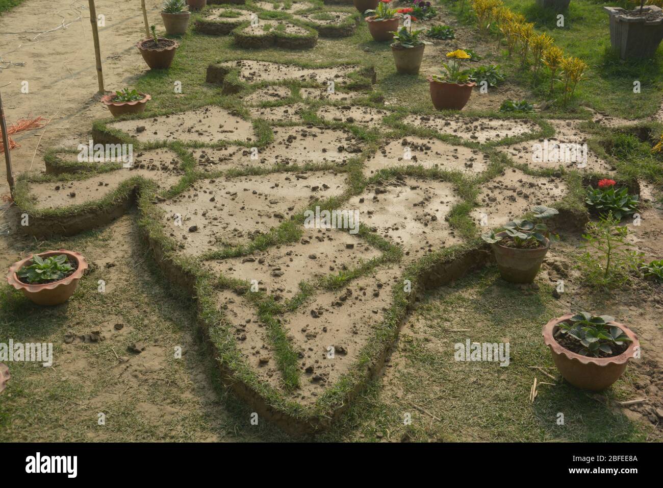 Close up of Indian and Sri Lankan map made on the ground with mud and boundaries with woven grass in a garden with flower pots Stock Photo