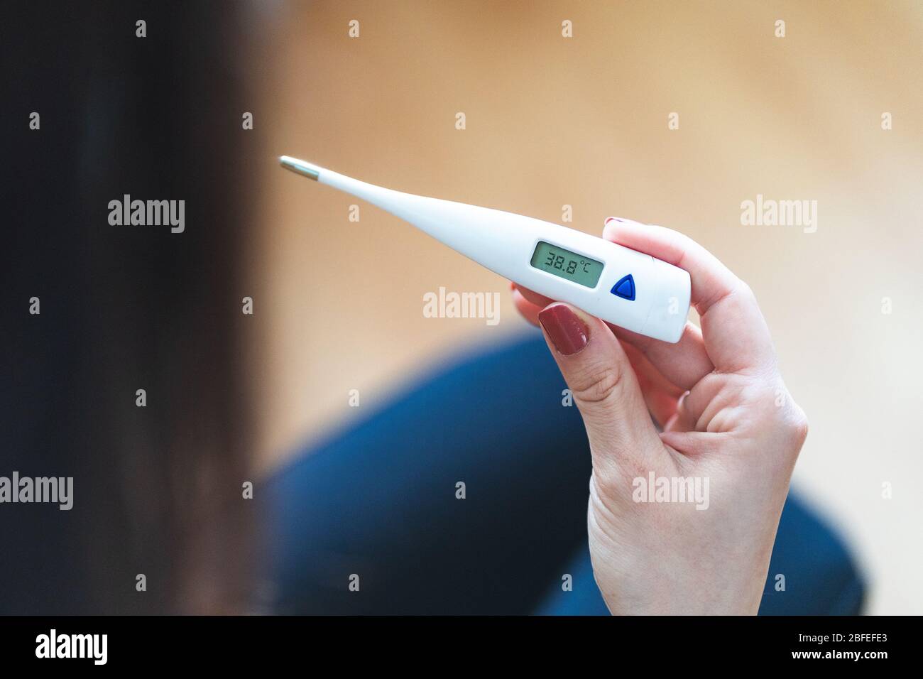 Selective focus of a woman holding a digital thermometer that indicates she has over 38 degrees fever. Sick and worried female with fever and illness Stock Photo