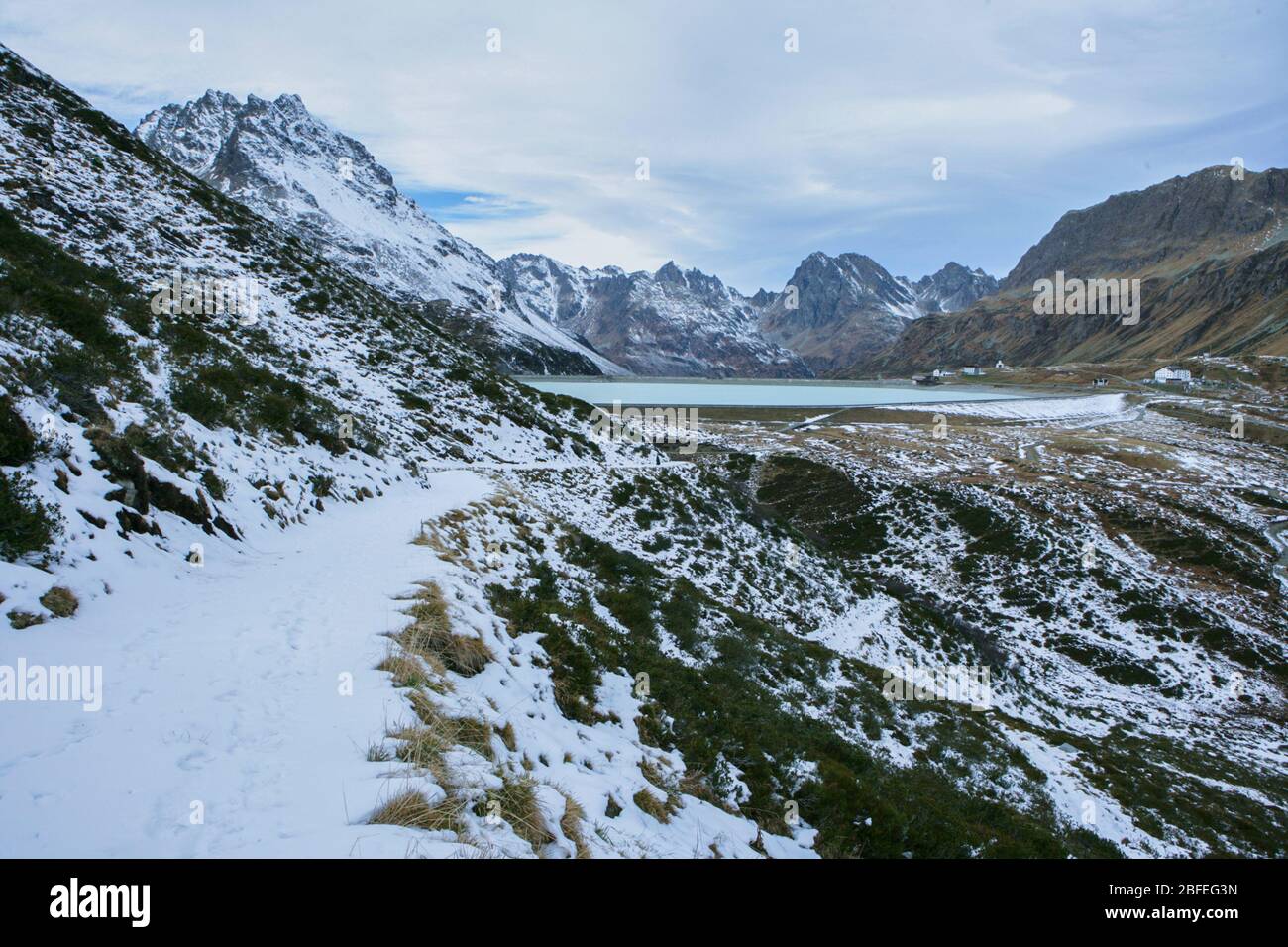 small hiking trail in the mountains with snow on the silvretta mountains with a view of the dam Stock Photo
