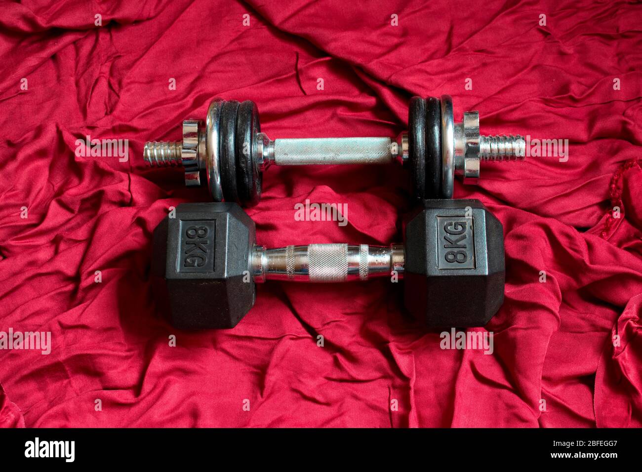 Two dumbbells are lying on red satin, ready for working out. Stock Photo