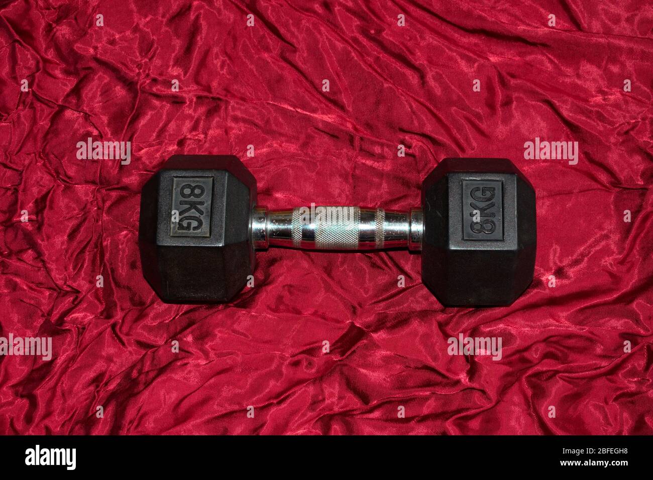 A dumbbell is lying on red satin, ready for working out. Stock Photo