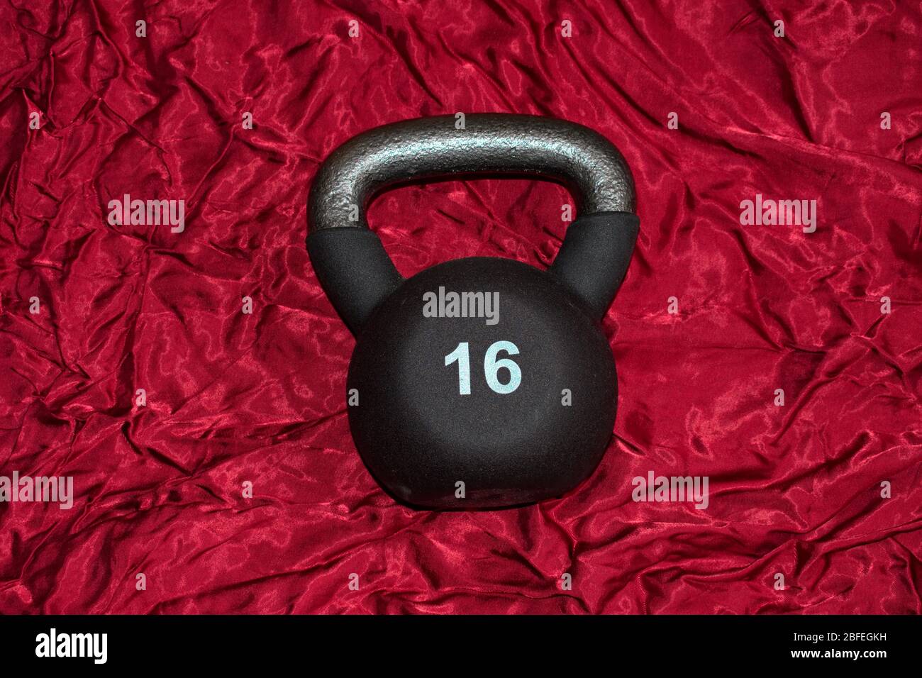 A 16 kg kettlebell is lying on red satin, ready for working out. Stock Photo