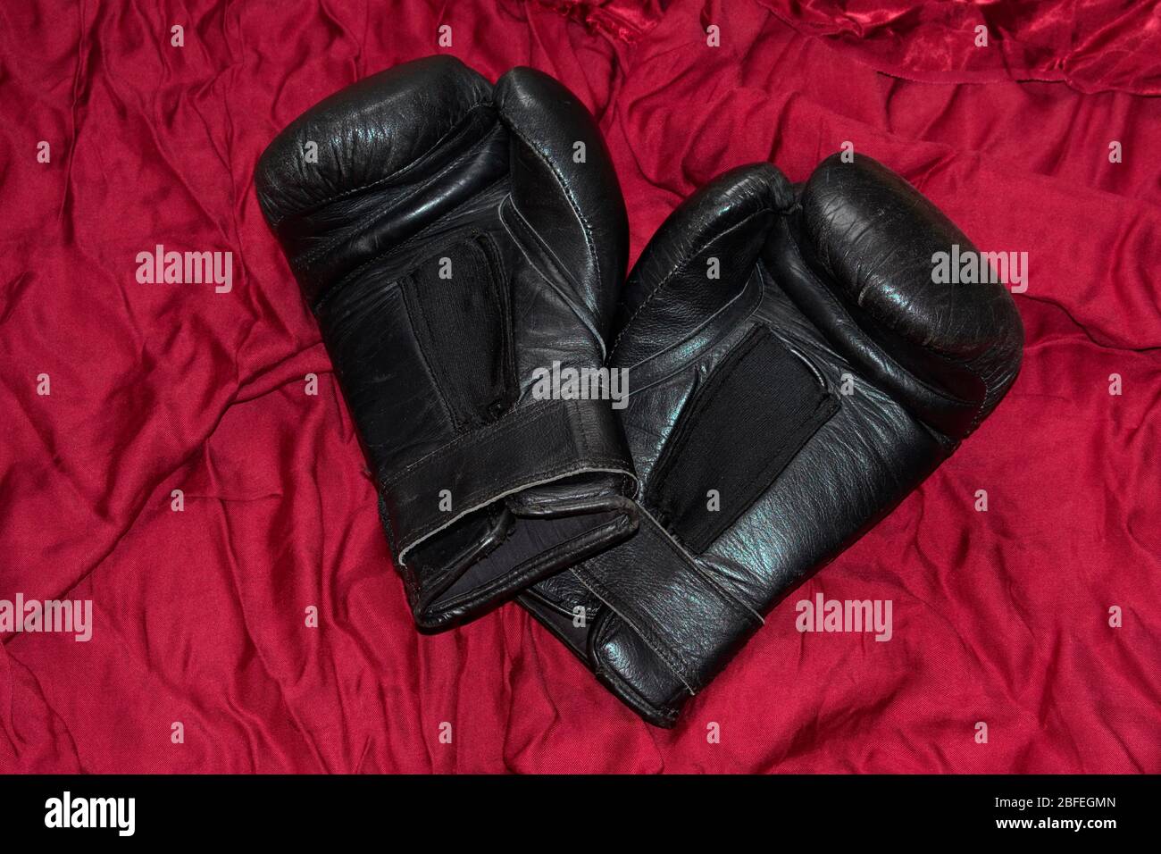 A pair of black leather boxing gloves i lying on red satin. Stock Photo