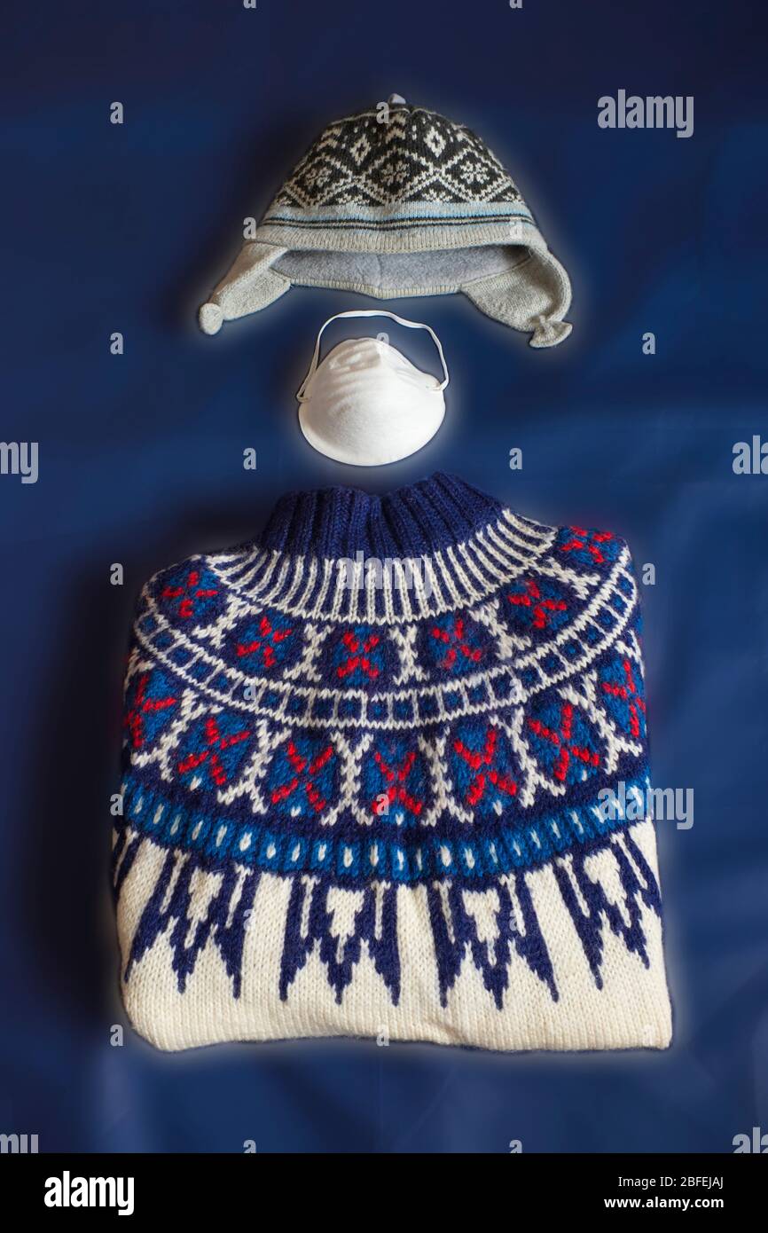 A hand-knit jumper, a knit cap and a face mask are spread out on a blue fabric. Stock Photo