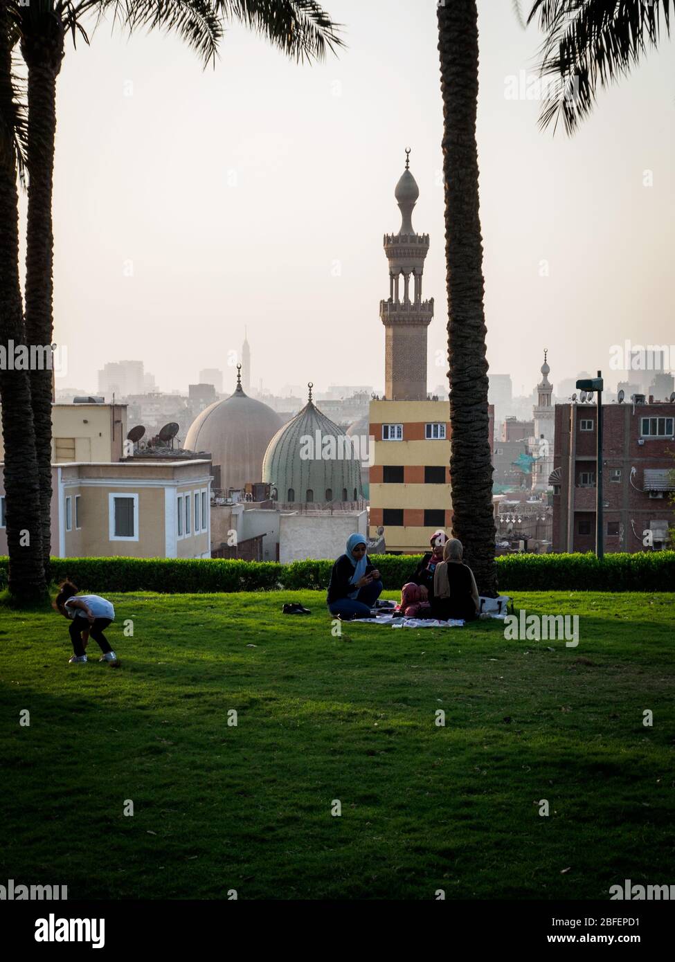 Al Azhar Park, Cairo, Egypt, October 2019, three girls sitting on the grass and a child playing with the skyline of cairo in the background Stock Photo