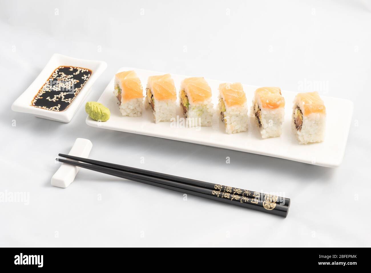 Sushi roll with pink salmon wrap, grilled salmon, Philadelphia cheese and avocado. White container and black chopsticks. Stock Photo