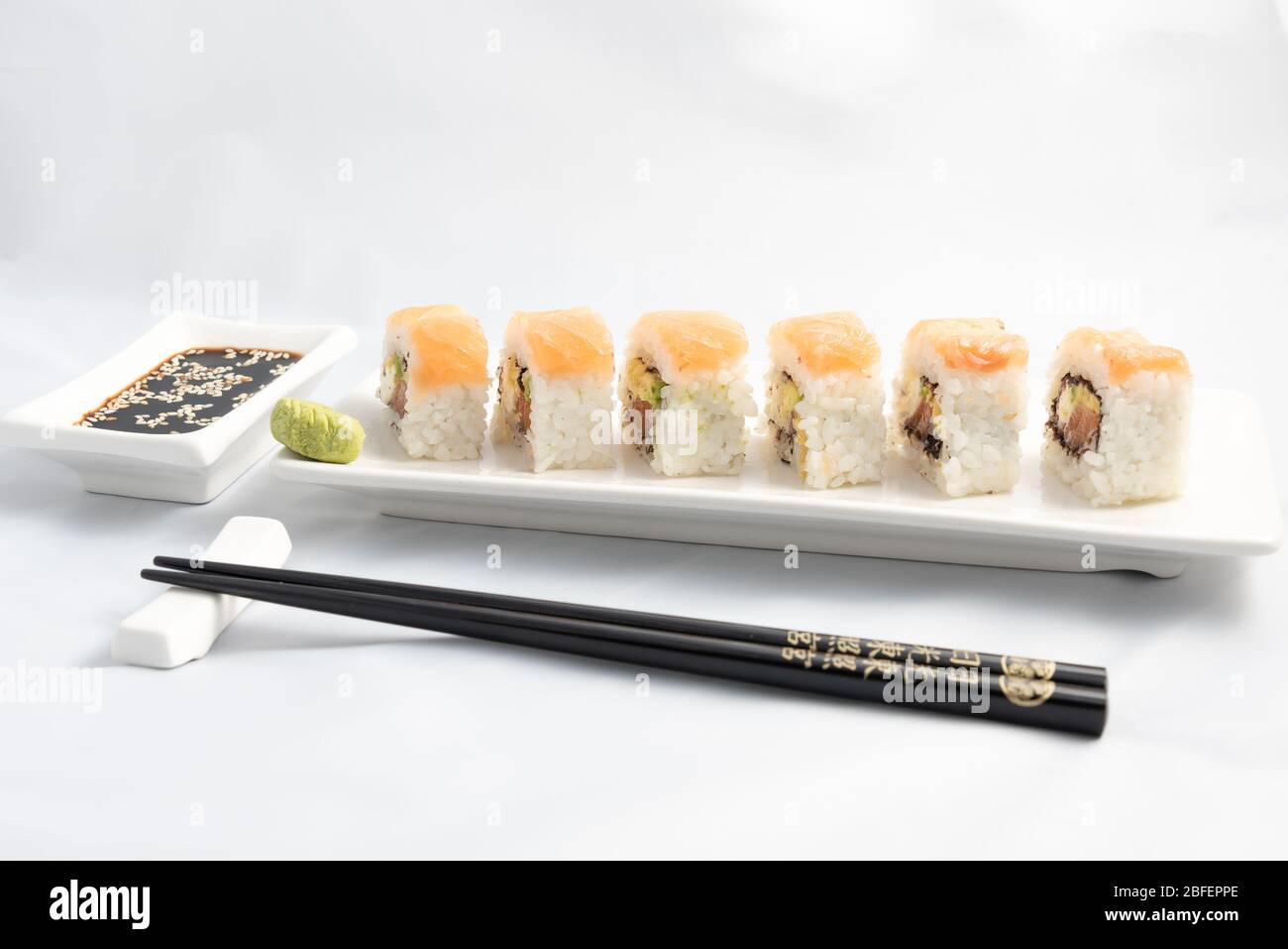 Sushi roll with pink salmon wrap, grilled salmon, Philadelphia cheese and avocado. White container and black chopsticks. Stock Photo