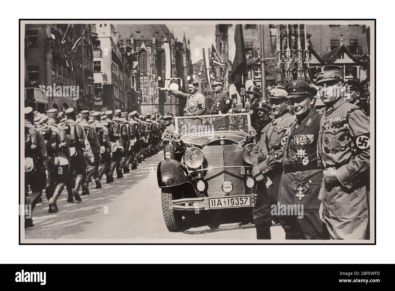 Vintage Nuremberg Rally 1935, Germany - SA Sturmabteilung political militia troops of the Nazi party, march past Adolf Hitler during a parade in the city. 1930’s Adolf Hitler wearing swastika armband in military parade, standing in Mercedes open car with Heil Hitler salute to passing marching Sturmabteilung troops Hermann Goring in foreground Nuremberg Germany Stock Photo