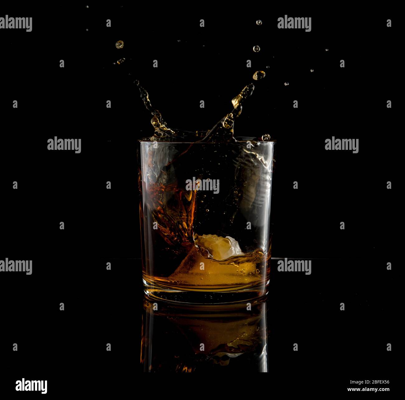 Splash in glass of whiskey and ice block falling on black background Stock Photo