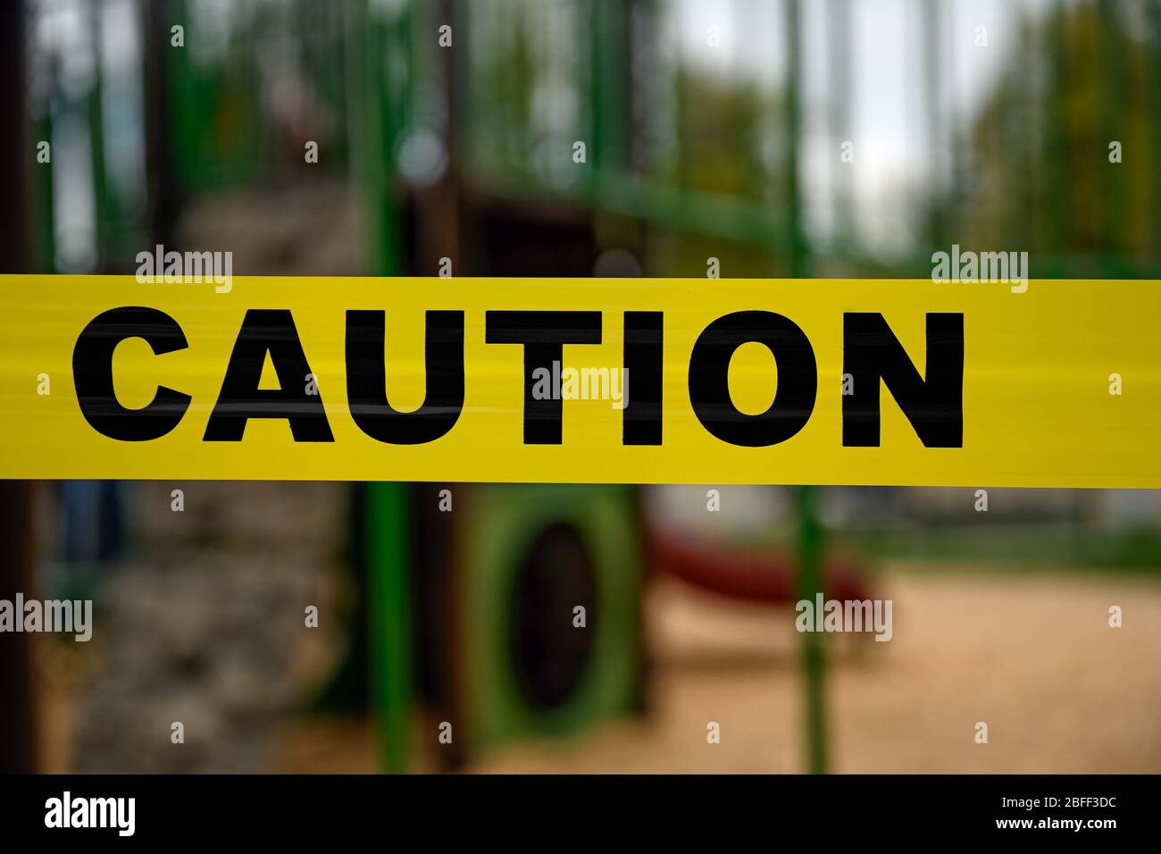 Yellow marker tape says Caution! Playground closed by health authorities due to Covid-19 pandemic. Stock Photo