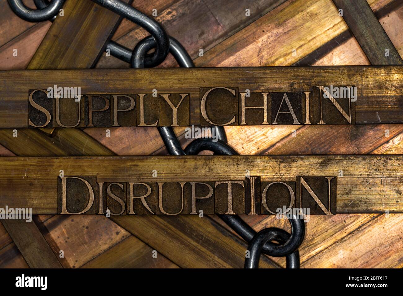 Photo of real authentic typeset letters forming Supply Chain Disruption text with steel chain on vintage textured grunge copper and gold background Stock Photo