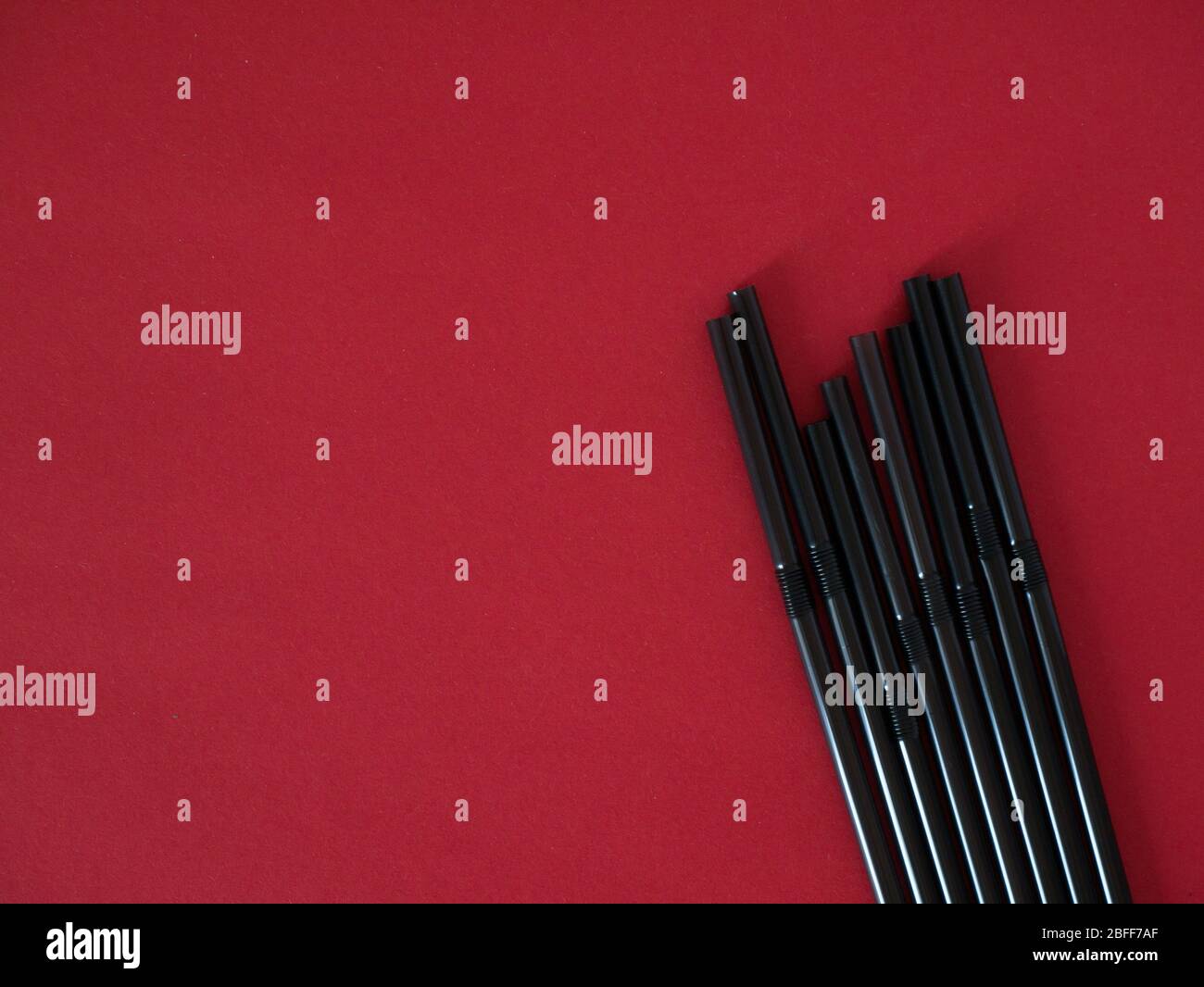 Black plastic single use straws isolated on red background. Top view. Stock Photo