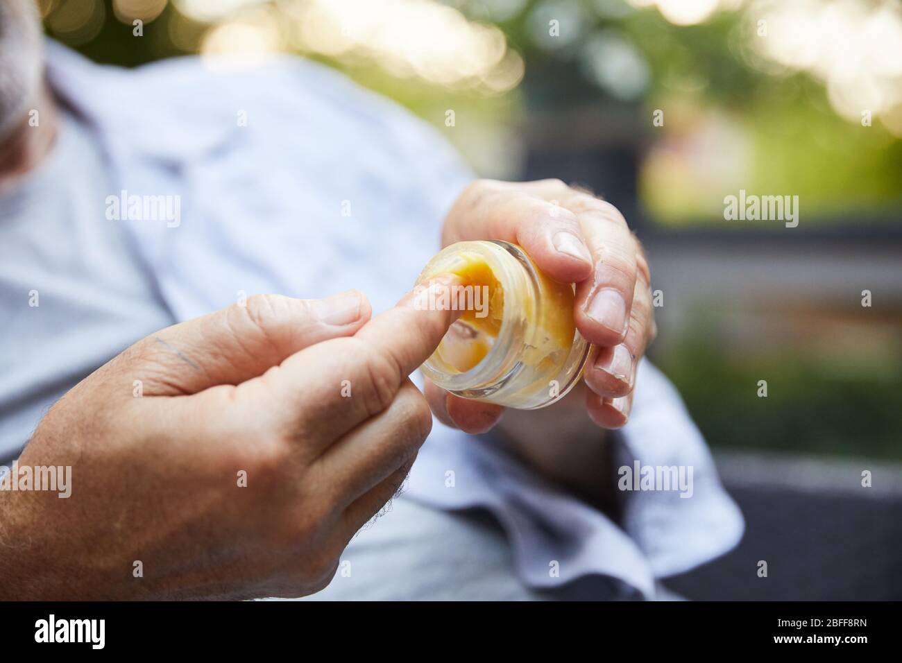 An older gentleman dips his finger in a jar of CBD oil before application for arthritis Stock Photo