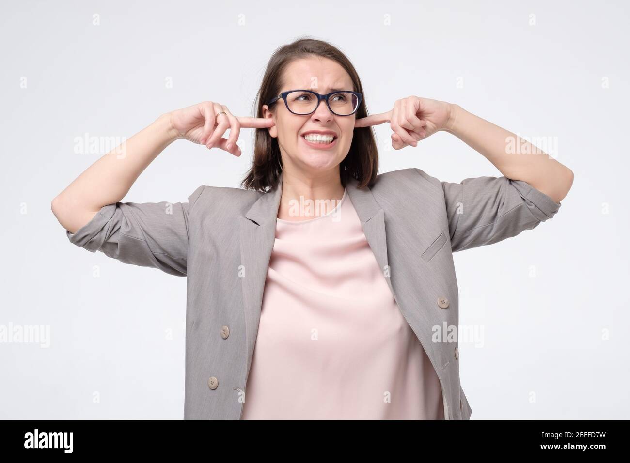 mature woman in glasses having discontent look plugging her ears being annoyed with noise wanting silence and calm atmosphere being exhausted Stock Photo