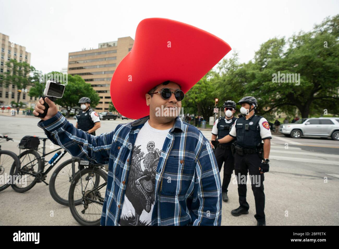 A man in an oversized cowboy hat watches a few hundred Texans flaunt social distancing guidelines during a 'You Can't Close America' rally at the Texas Capitol. Texas State Troopers look on behind him. Stock Photo