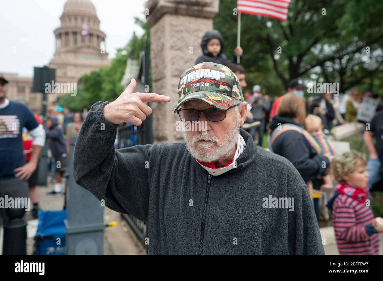 A man pointing to his 'Trump 2020' hat joins a few hundred Texans flouting social distancing guidelines at the Texas Capitol during a 'You Can't Close America' rally encouraged by the alt-right website Infowars. Attendees protested government policies aimed at slowing the spread of the coronavirus as overly restrictive and a violation of Americans' constitutional rights. Stock Photo