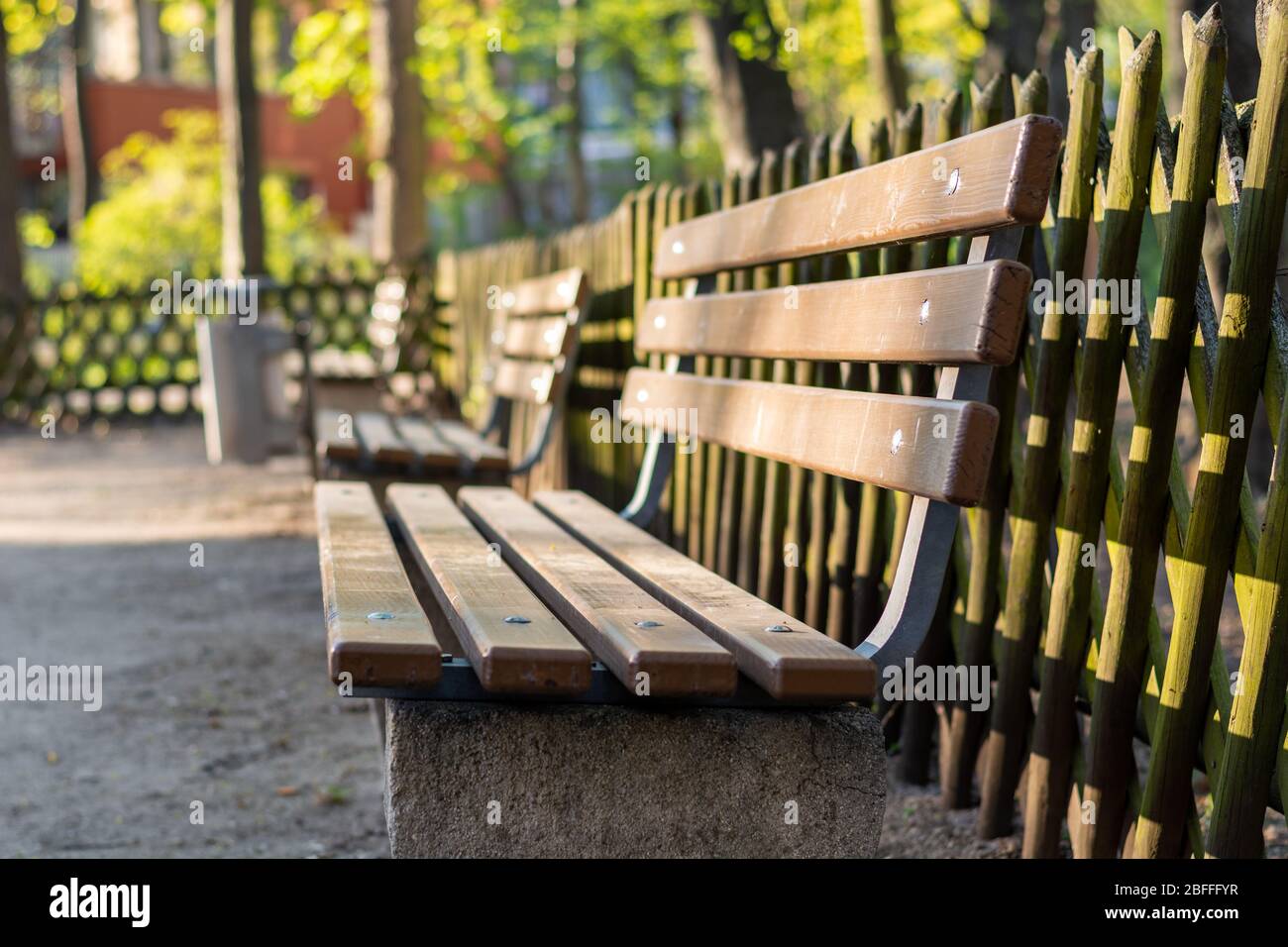 A wooden bench in a park with a wooden fence behind it from the side ...