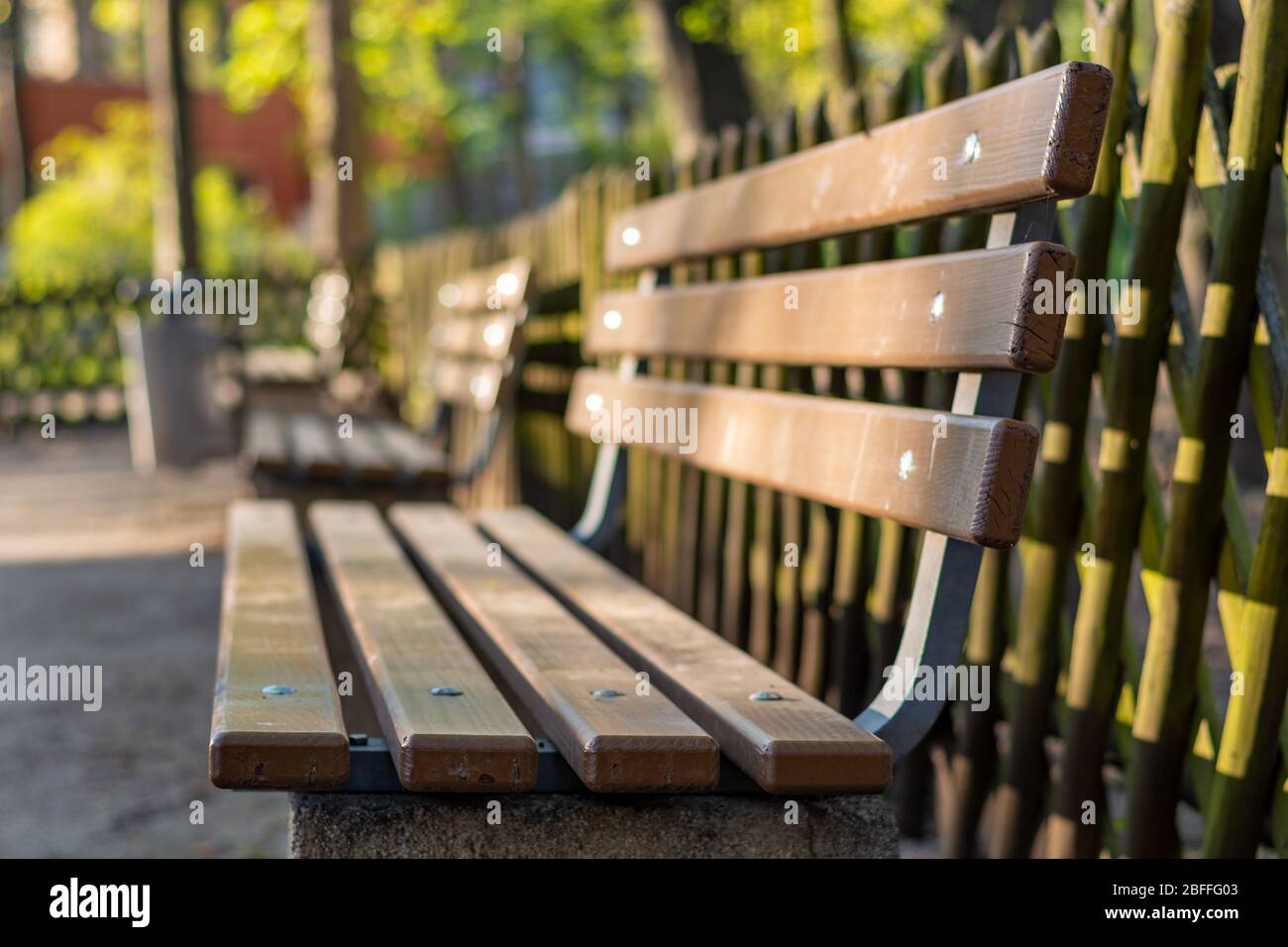 A wooden bench in a park with a wooden fence behind it from the side ...