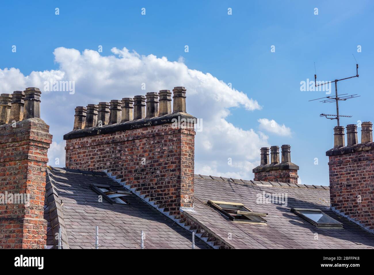 Rows of chimney pots on brick built chimneys on a slate roof with TV arial. Stock Photo