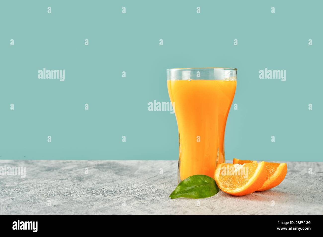 Glass of fresh orange juice with oranges on green-blue background Stock Photo