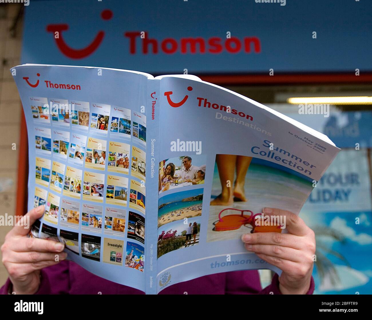 A woman browses a travel brochure outside a branch of Thomson travel agency. Stock Photo