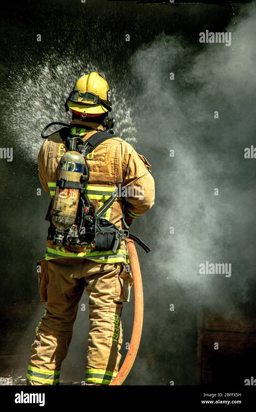 Wearing breathing equipment, a fireman sprays water in a structure fire demonstration by the Costa Mesa, CA, fire department. Stock Photo