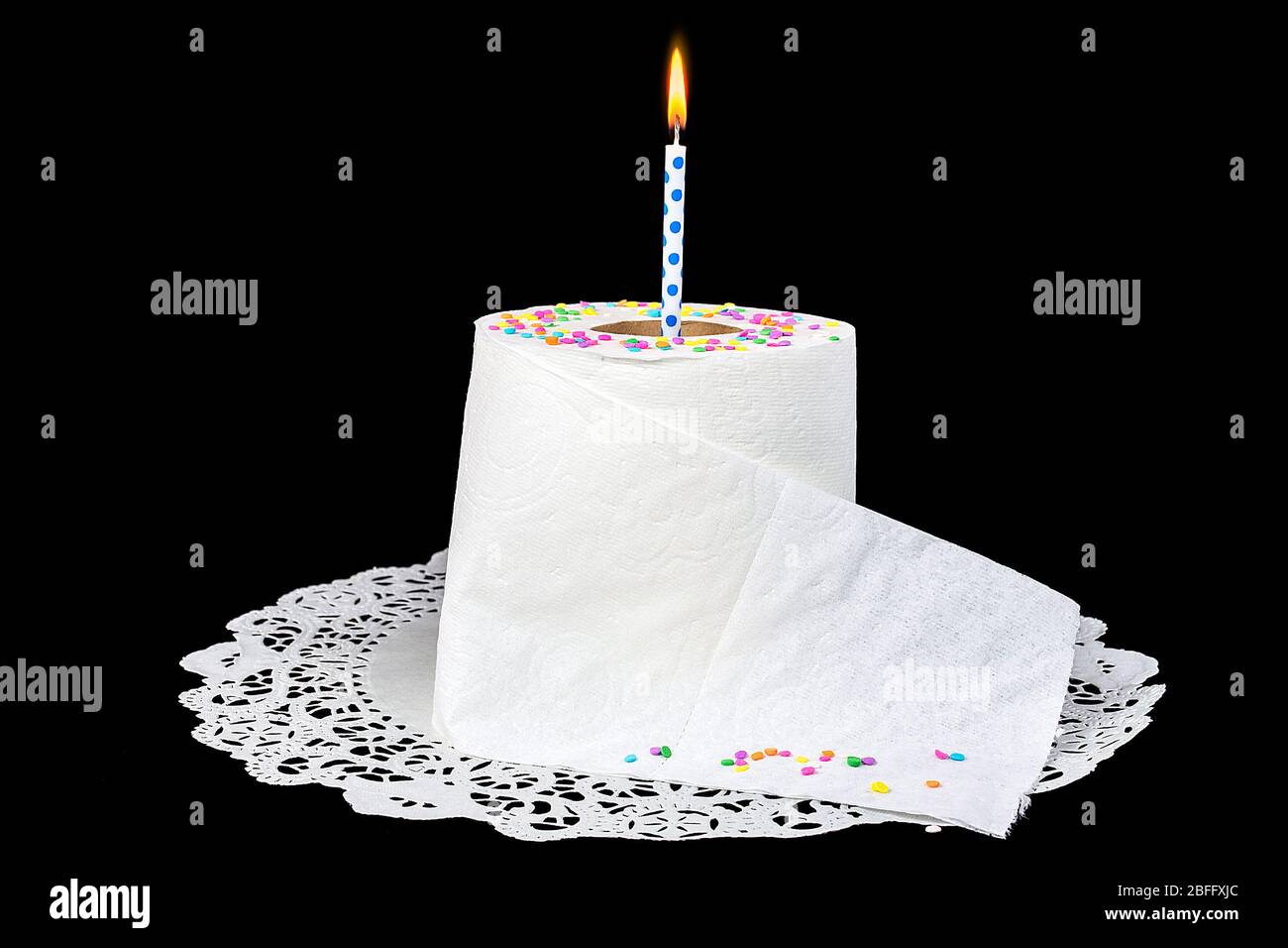 birthday candle in roll of toilet paper on lace paper doily with candy confetti sprinkles Stock Photo