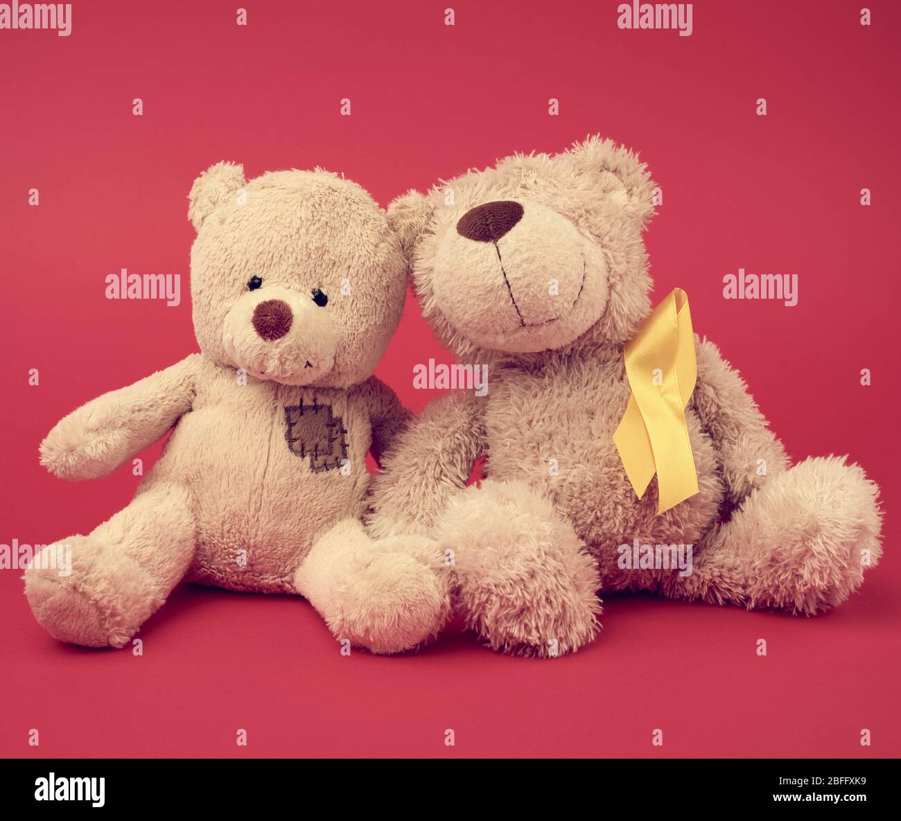 brown teddy bear and a silk yellow ribbon in the shape of a loop on a red background, concept of the fight against childhood cancer, problem of suicid Stock Photo