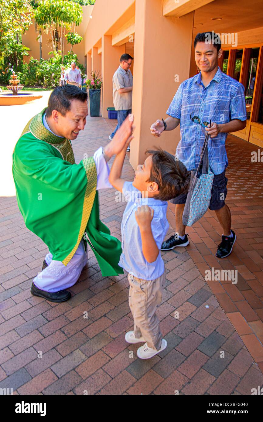 A robed Vietnamese American priest gives a high five to an enthusiastic young parishioner after mass at a Southern California Catholic church Stock Photo