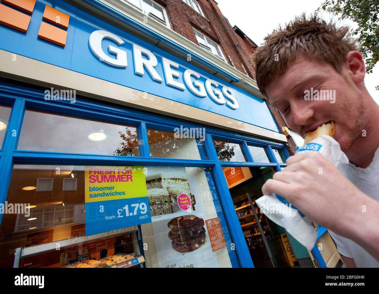 A man enjoys a sausage roll outside a branch of Greggs the Baker Stock