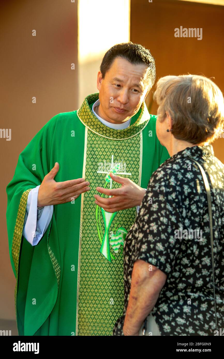 A robed Vietnamese American priest chats with a parishioner after mass at a Southern California Catholic church. Stock Photo