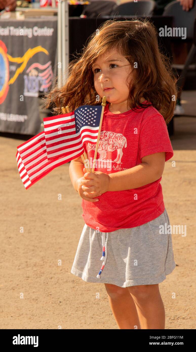 A two-year-old girl displays a trio of US flags as she watches a patriotic group observance in Costa Mesa, CA. Stock Photo