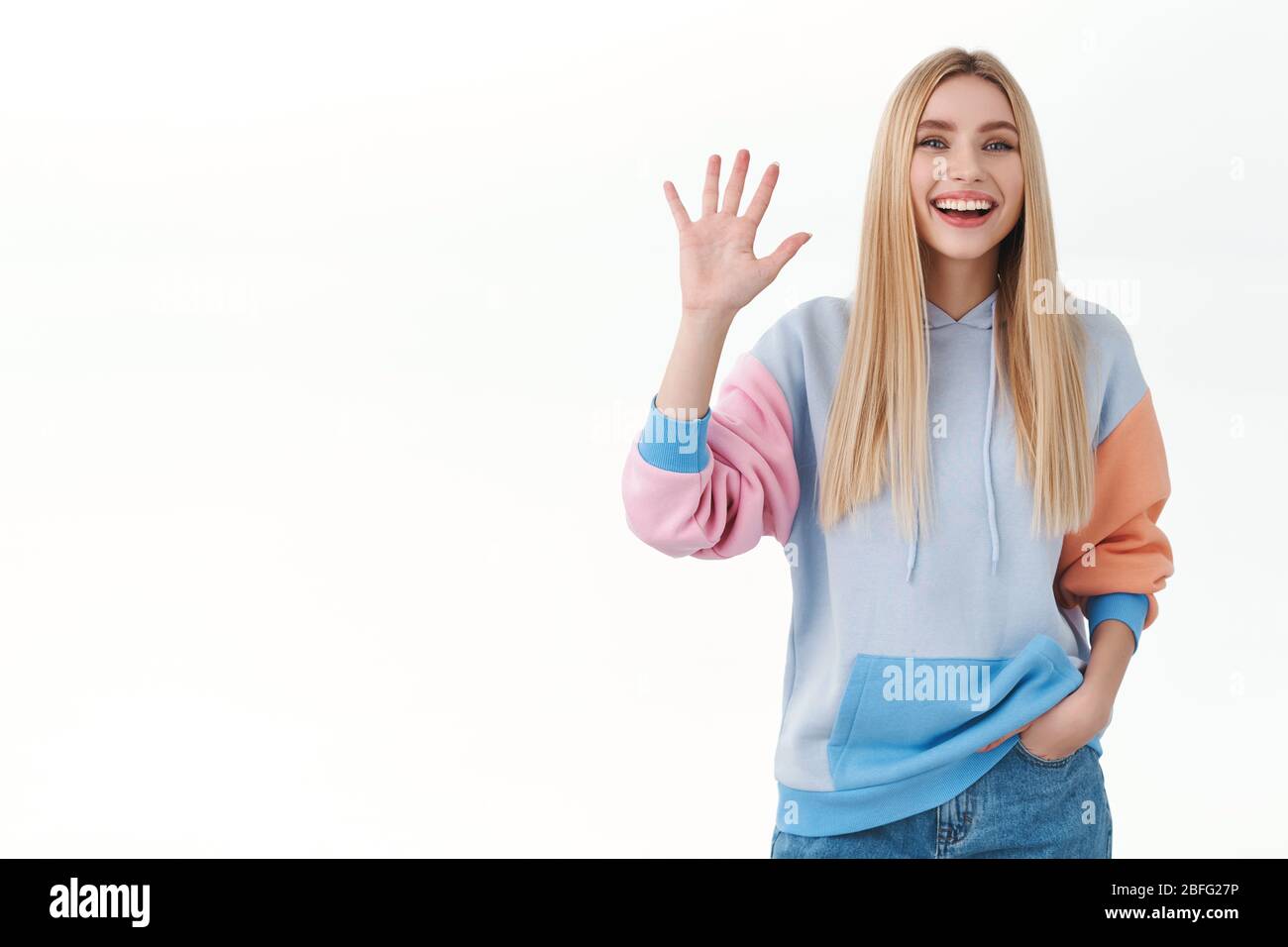Friendly cheerful blonde girl smiling broadly, say hi and waving hello,  greeting friends with casual carefree attitude, standing white background  Stock Photo - Alamy, image size:1300x956