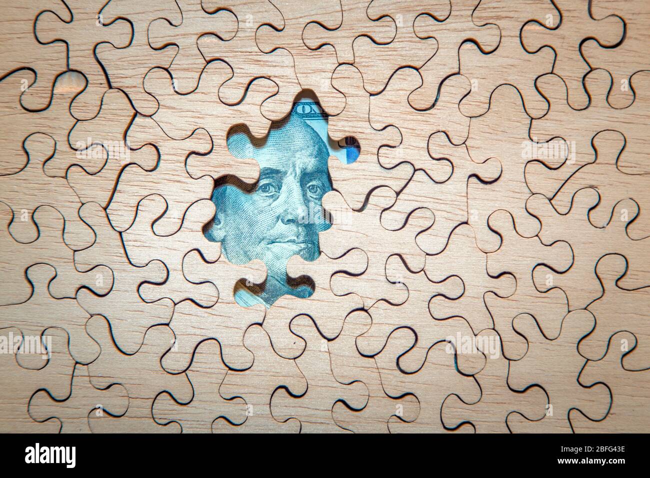 Benjamin Franklin on the $100 bill peeks through an unfinished jigsaw puzzle. Stock Photo
