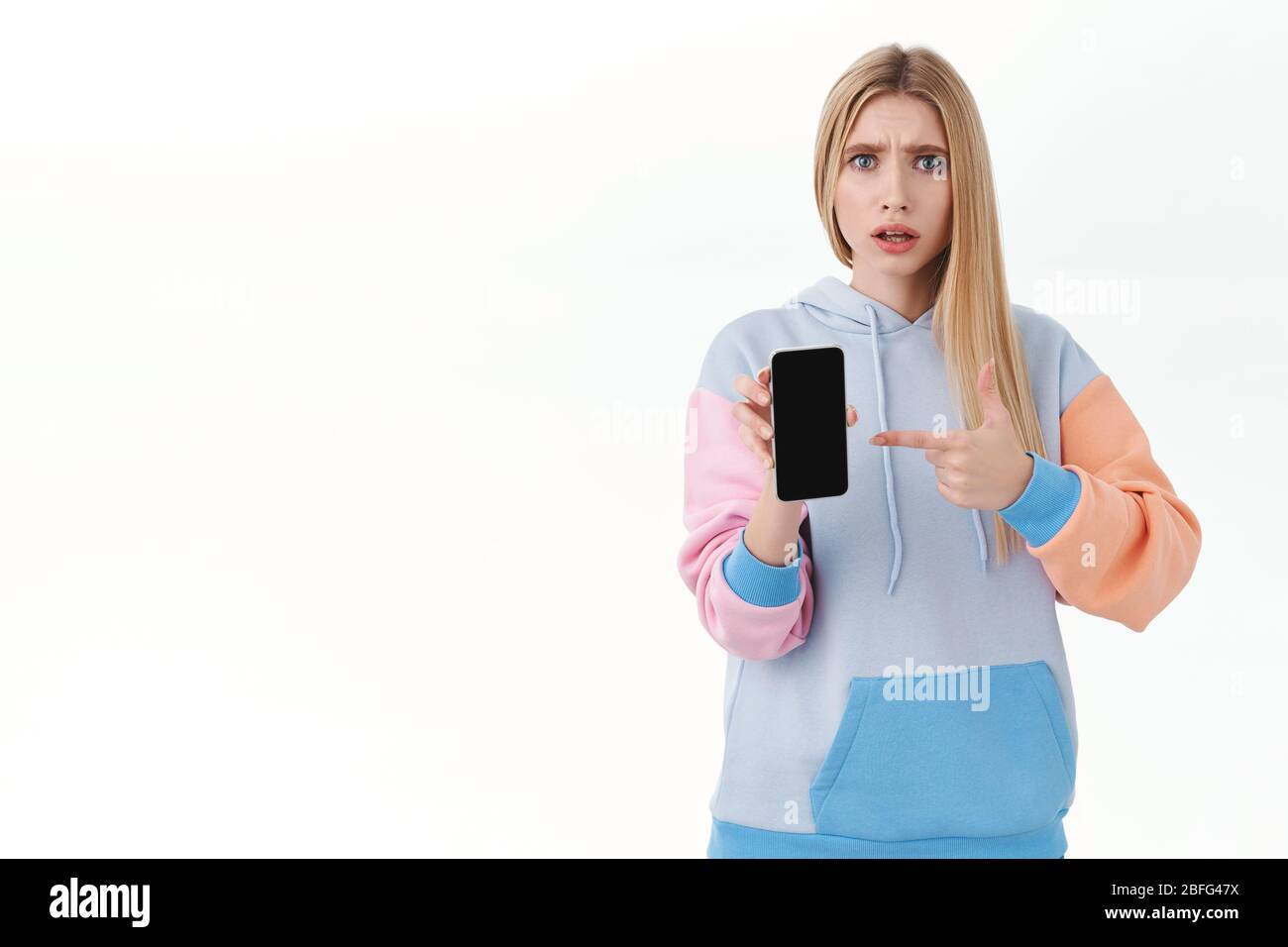Communication, smartphone and promo concept. Portrait of frustrated blond girl being confused with strange bad news on media, pointing at mobile phone Stock Photo