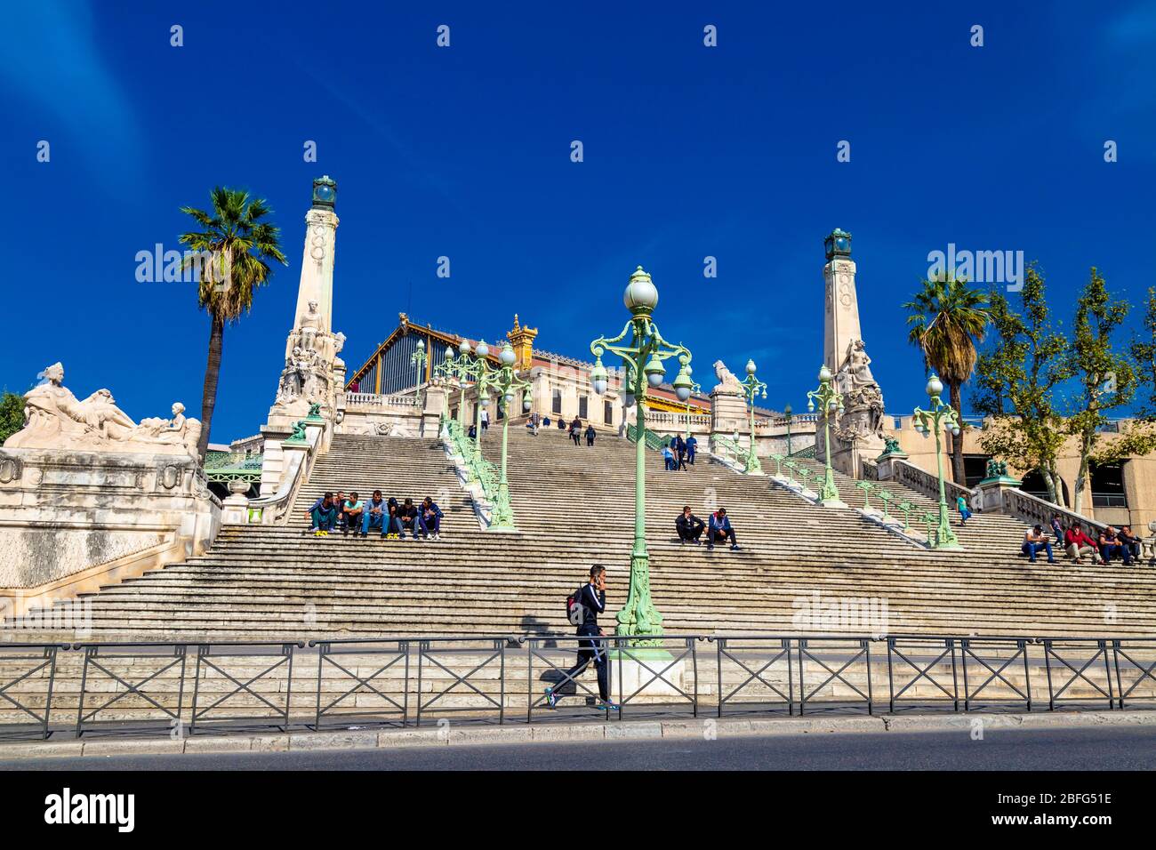 People sitting on stairs outside train station building Gare de Marseille-Saint-Charles, Marseille, France Stock Photo