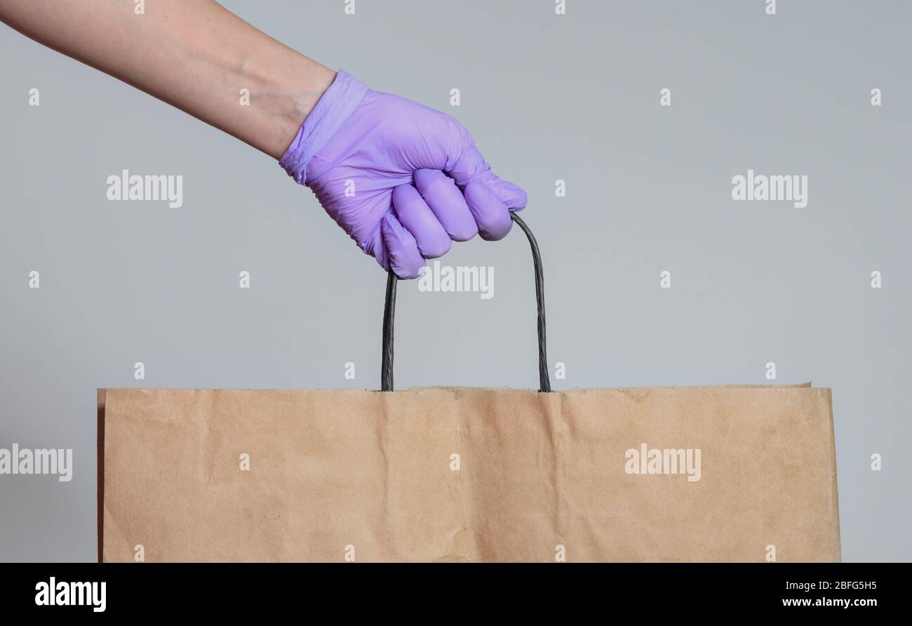 Woman's hand with surgical glove holding a paper brown bag on a gray ...