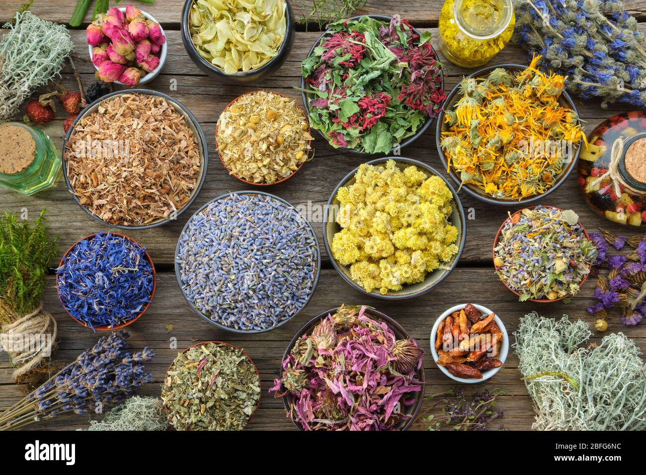 Bowls of dry medicinal herbs - lavender, coneflower, cornflower, marigold, rose, Helichrysum flowers, healthy moss and lichen, infusion bottles. Top v Stock Photo