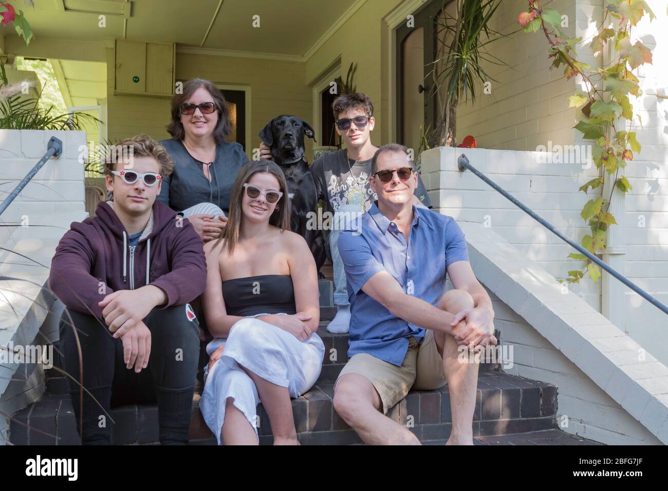 A smiling Australian family of husband wife daughter and two sons plus pet  dog all wearing sunglasses, sit at the front steps of their Sydney home  Stock Photo - Alamy